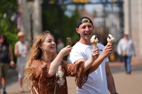 Couple taking a selfie with ice cream cones in a park.