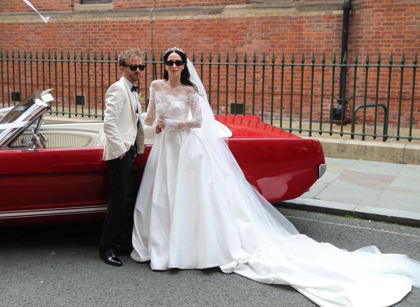 Newlyweds Jack P. Shepherd and Hanni Treweek by their red Mustang.