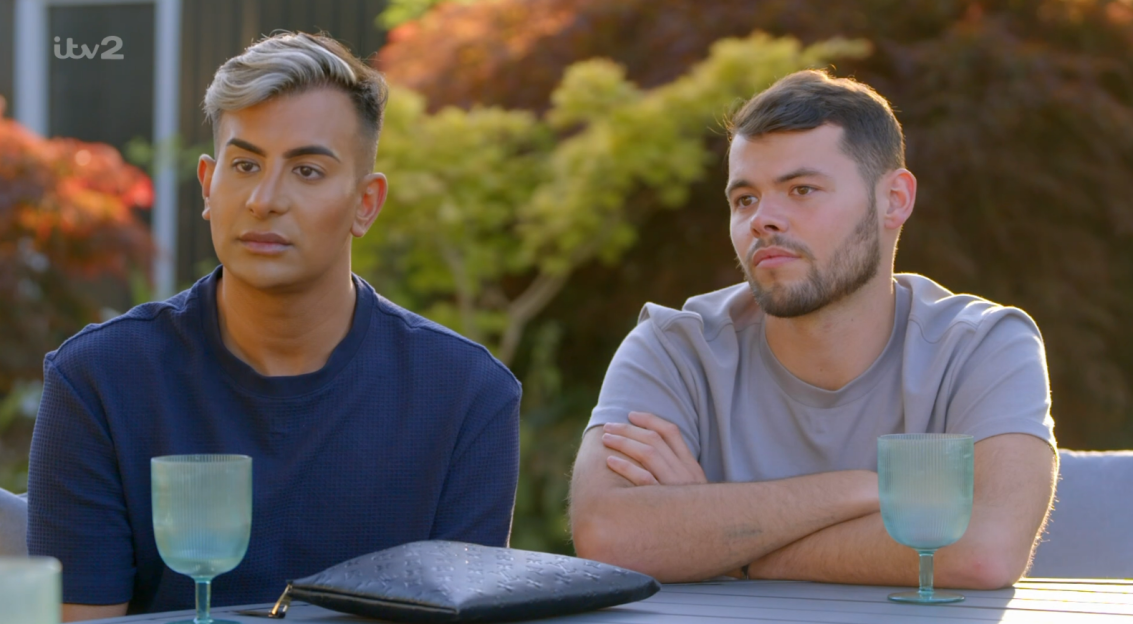 Screenshot of two men sitting outdoors at a table.