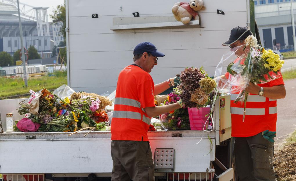 Two workers placing floral tributes into the back of a truck.
