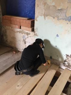 Woman installing floorboards in a dilapidated room.