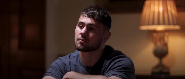Man in a dark shirt sits and looks thoughtfully to the side.