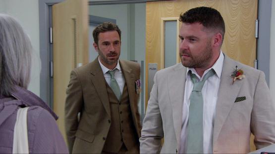 Two men in suits, one in brown and one in beige, appear to be having a conversation.