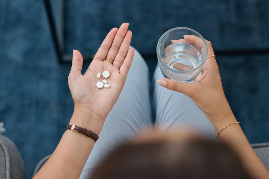 Person holding pills and a glass of water.