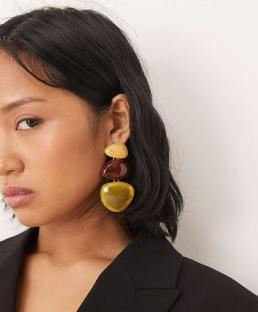 Woman wearing three-stone drop earrings in yellow, brown, and green.