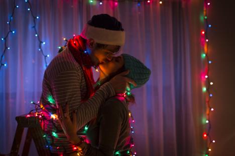 Young couple kissing at Christmas, surrounded by Christmas lights.