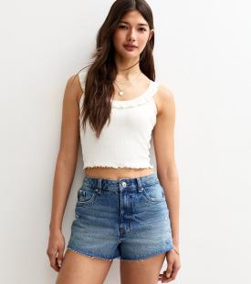 Woman wearing denim shorts and a white ruffled tank top.