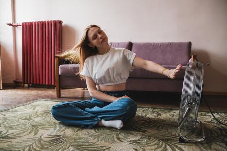 Young woman sitting on the floor cooling down with an electric fan.
