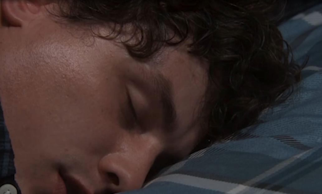 Close-up of a person sleeping, with their eyes closed and face resting on a plaid pillow.