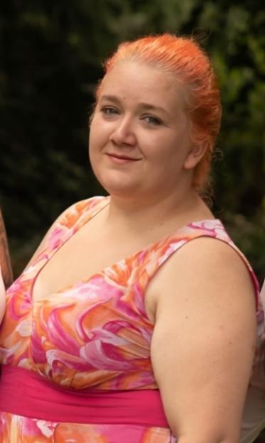 A woman with orange hair smiling slightly.