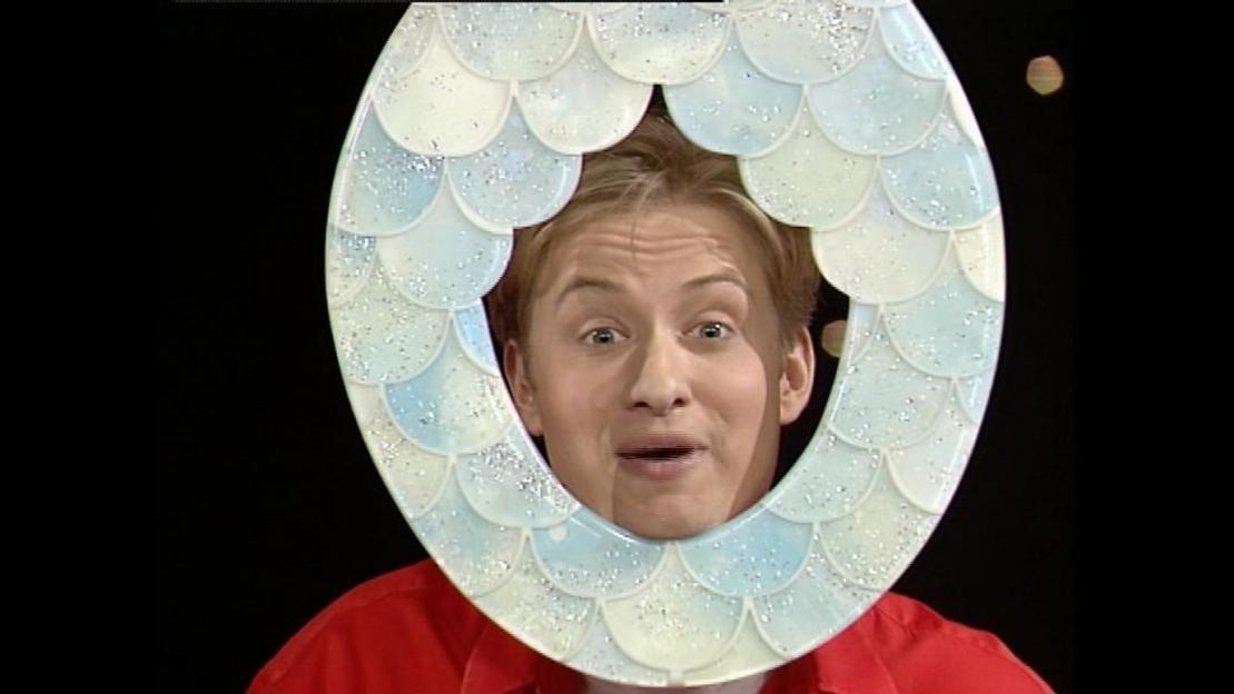 A man with blond hair puts his head through a decorative toilet seat.