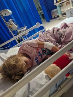 A young girl sleeping in a hospital bed with a teddy bear.