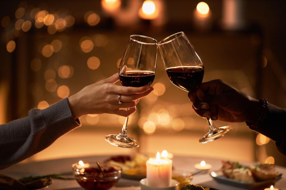 Two people clinking wine glasses at a candlelit dinner.