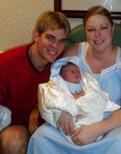 a man and woman holding a baby wrapped in a white blanket