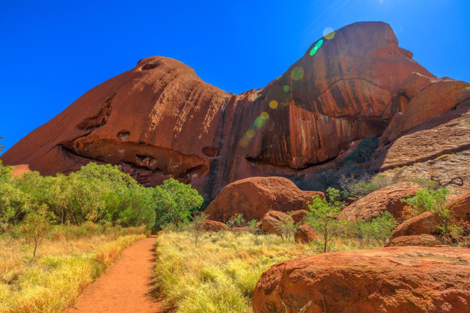 Red sand path leading to Uluru rock formations.
