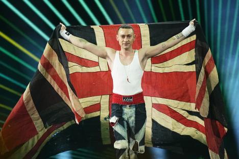 Olly Alexander holding a large UK flag on stage.
