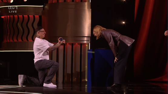 Screenshot of a man proposing to a woman on a game show stage.