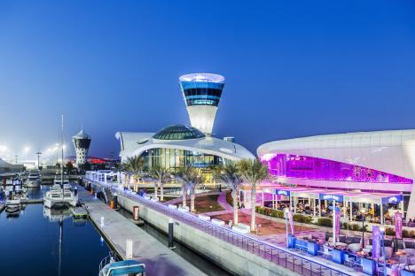 Night view of Yas Marina in Abu Dhabi, with yachts moored and illuminated buildings.