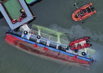 Aerial view of a capsized passenger boat with rescue workers in inflatable boats.