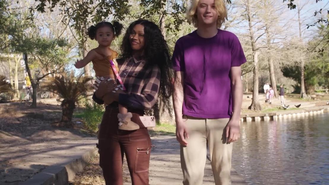 Woman carrying a baby, walking with a man in a park.