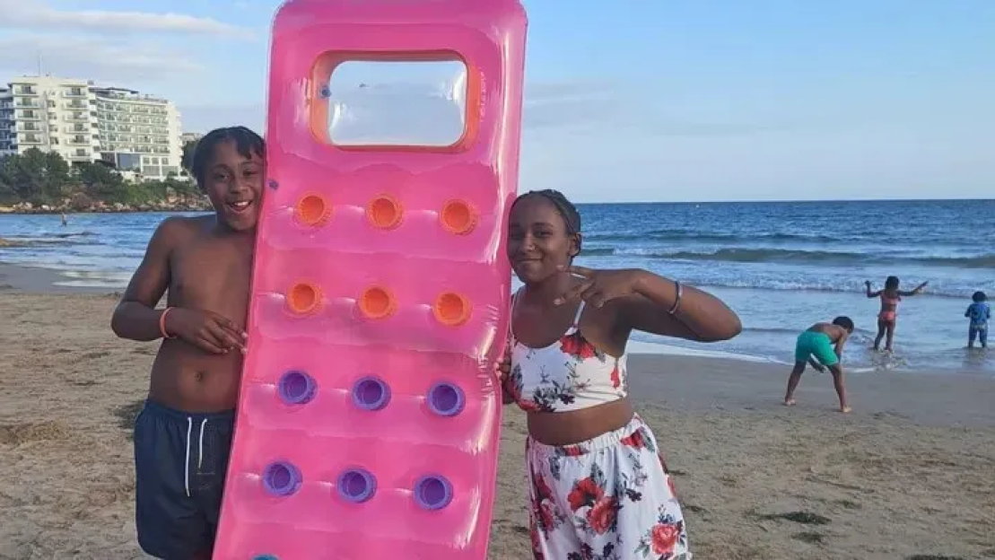 Two children on a beach with a pink inflatable raft.