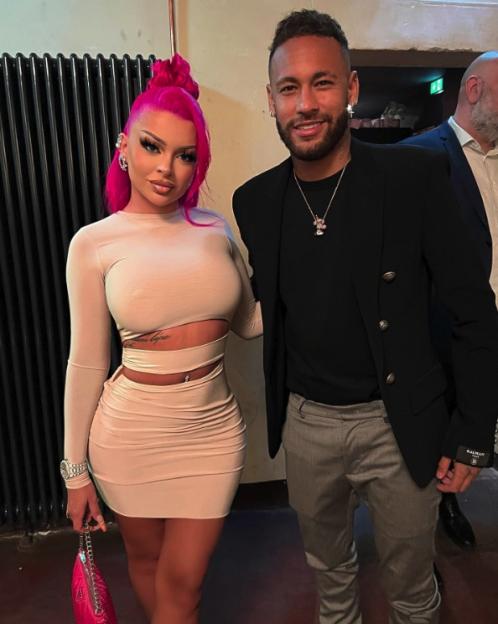 A woman with pink hair in a beige dress standing next to a man in a black jacket.