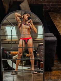 Man taking a selfie in a mirror wearing a harness and jockstrap.