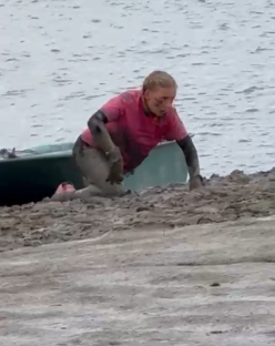 Person covered in mud crawling out of the water.