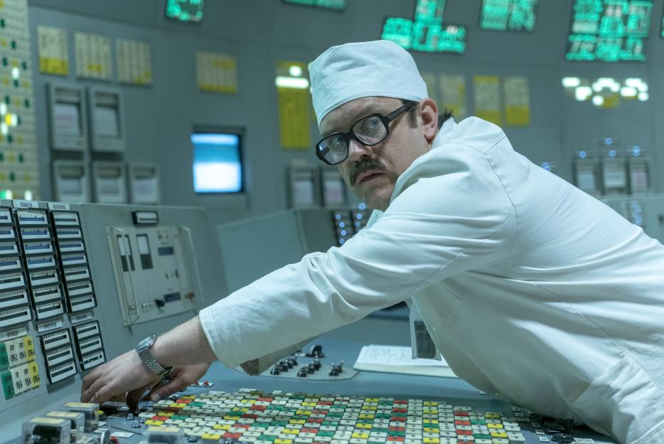 Man in a white lab coat operating a control panel.