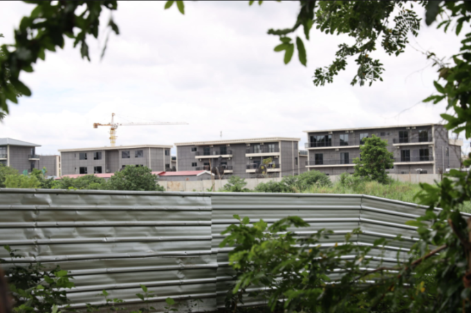 A notorious scam compound in Myanmar, a series of identical grey buildings seen from behind a corrugated metal fence.