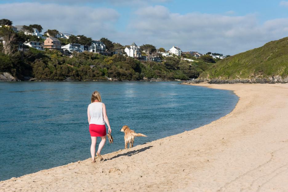 EX9J2J A holidaymaker wand her dog walking along the bank of the River Gannel on Crantock Beach in Newquay, Cornwall.