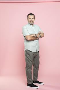 Man with arms crossed, standing against a pink background.