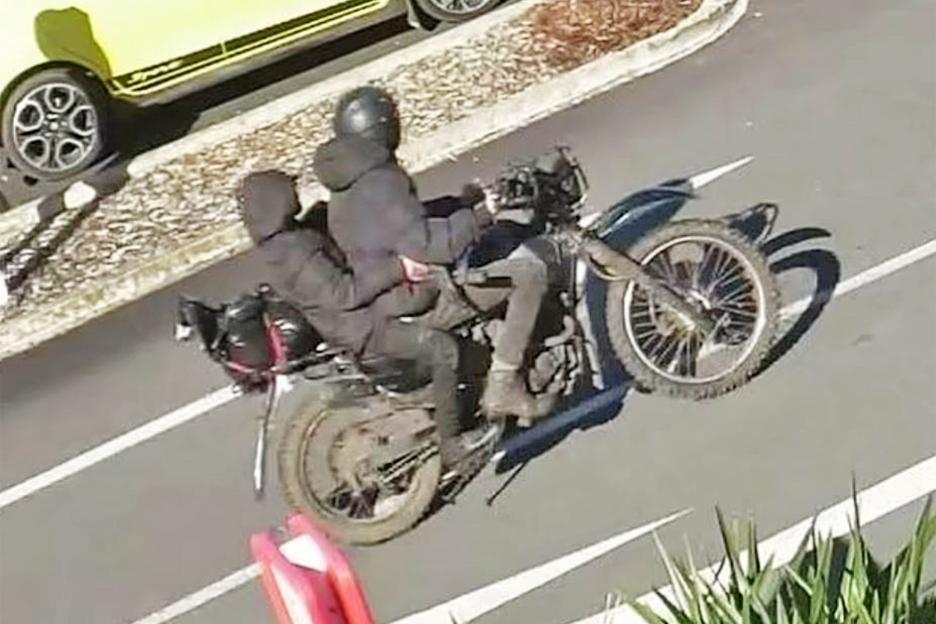 Black motorbike with two people riding away from a bank robbery.