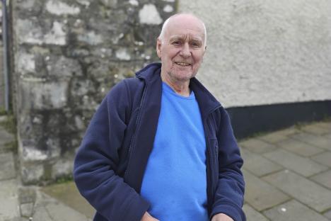 Portrait of a smiling older man wearing a blue shirt and dark jacket.