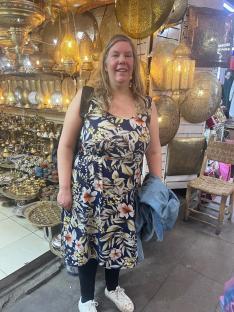 Woman in floral dress in Marrakesh market surrounded by brass lamps.