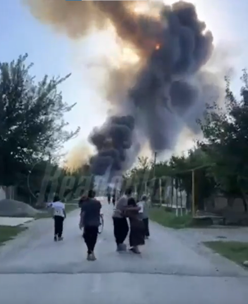People evacuating as a large fire burns in the distance.