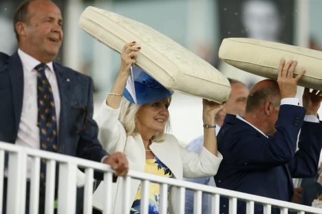 Racegoers using cushions as rain shields at a horse race.