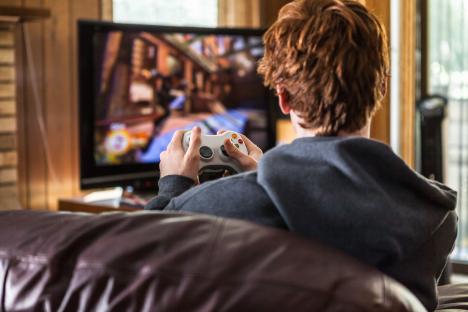 A redhead teenager plays a video game on a large screen TV.