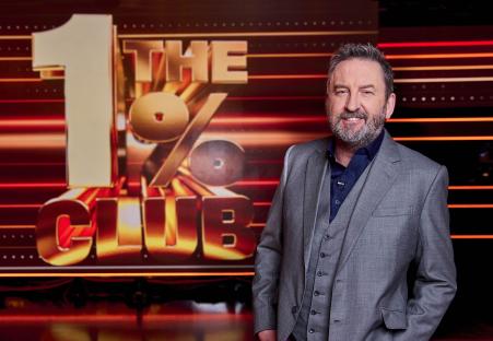 Lee Mack in a suit, standing in front of the