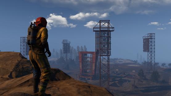 A person in a hazmat suit looks toward rusty industrial structures.