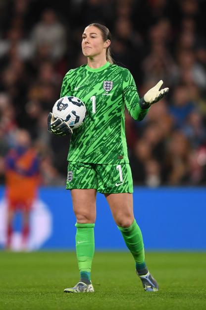 England goalkeeper Mary Earps in a green uniform and gloves, holding a soccer ball at Wembley Stadium.