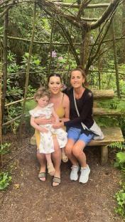A grandmother, her daughter, and granddaughter sitting on a wooden bench in a garden.