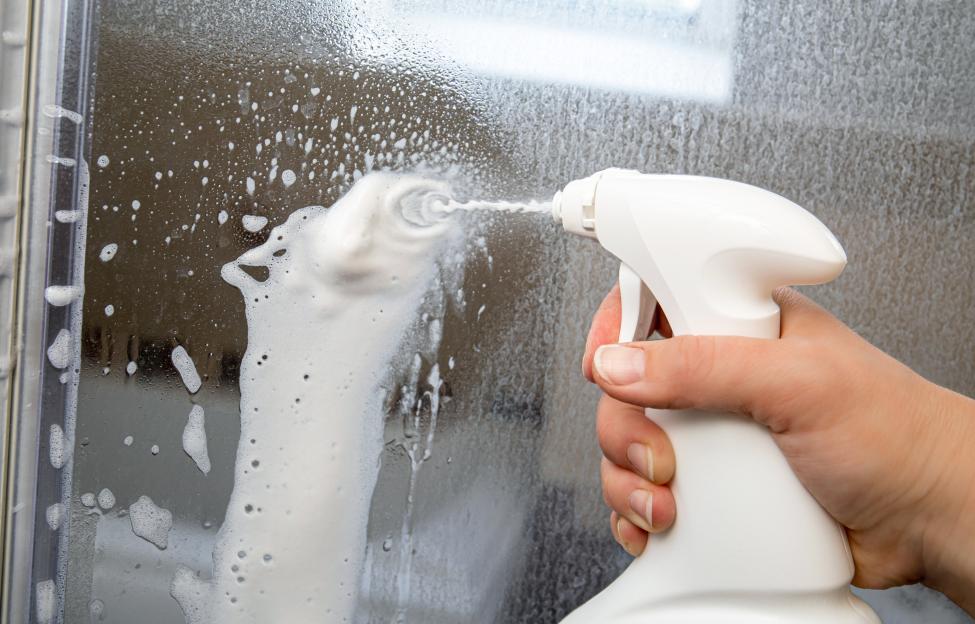 Person cleaning shower glass door with limescale remover.