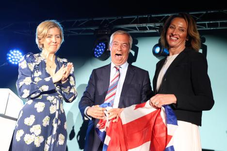 Nigel Farage with two Reform UK election winners holding a UK flag.