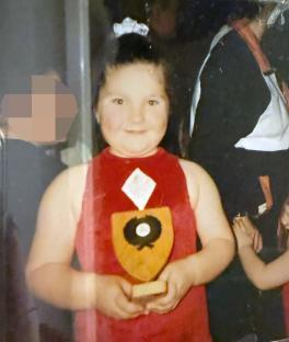 Photo of a young girl in a red dress holding a trophy.