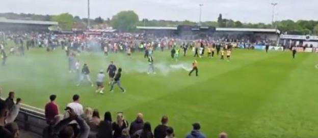 Crowd on a soccer field with smoke and flares.