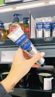 Hand holding tube of D'Avignon shea hand cream in a supermarket.
