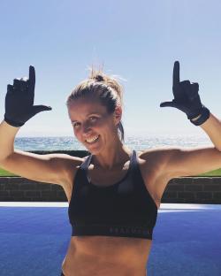Woman in sports bra making hand gestures by a pool.