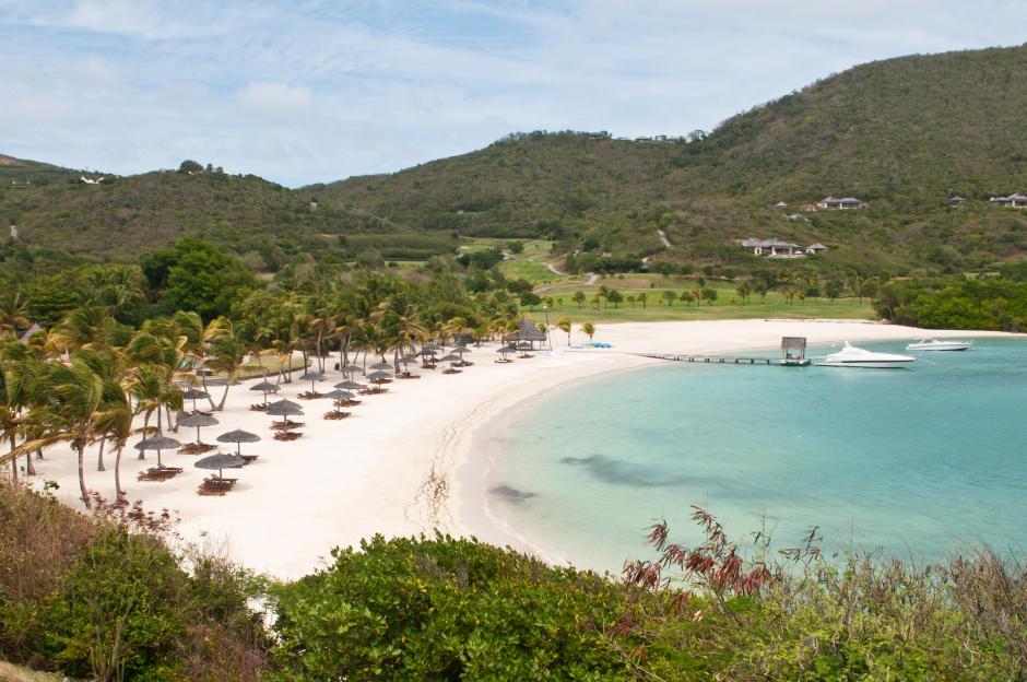 Canouan Resort at Carenage Bay with palm trees, beach chairs, umbrellas, and yachts.