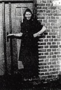 a black and white photo of a woman standing in front of a brick wall .